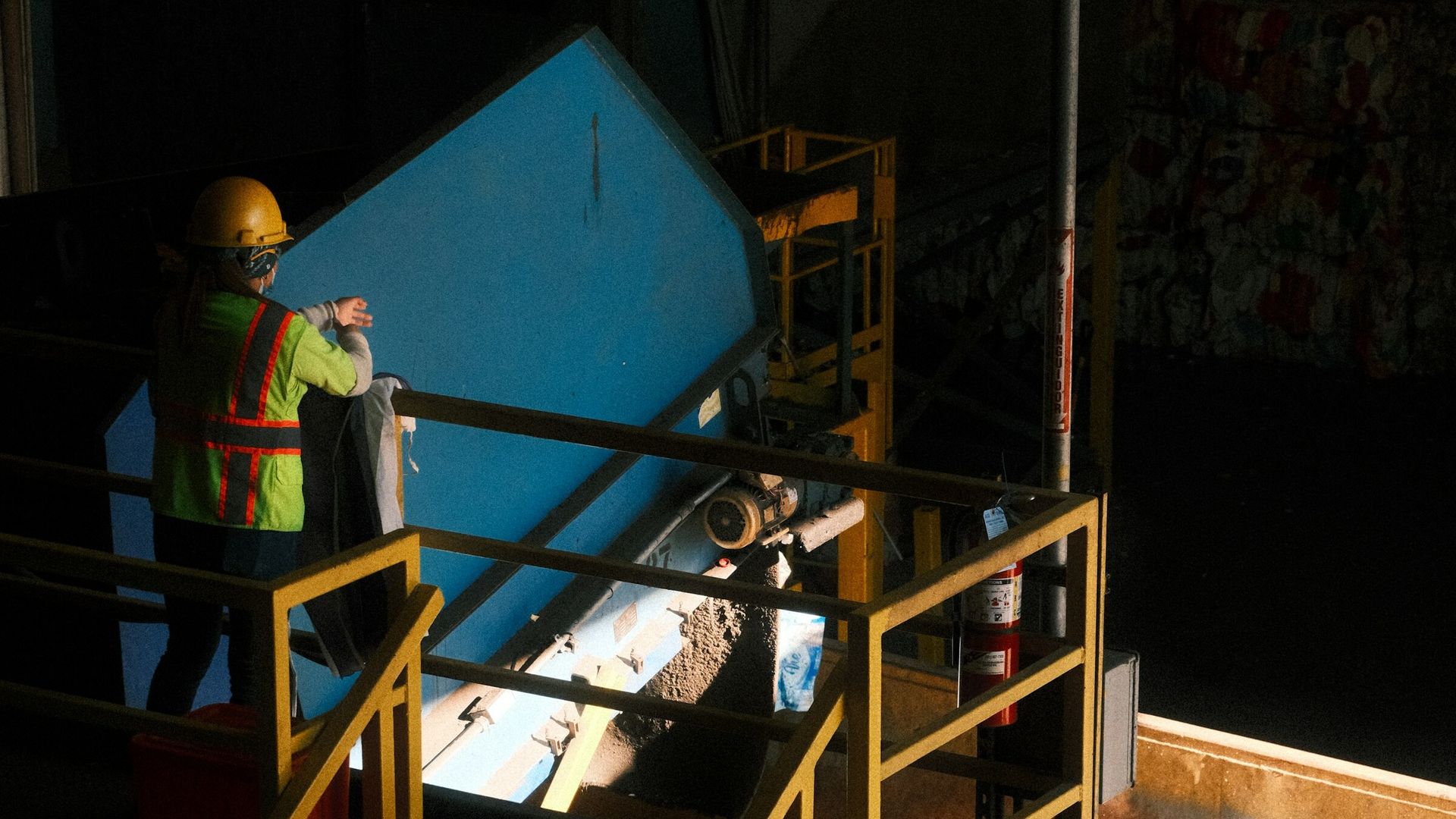 Scott Plastics worker feeding sorted plastic onto the recycling conveyor line, baled material in the background